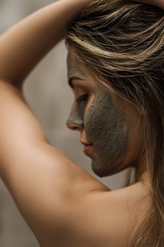 Woman applying a clay facial mask with hands in her blonde hair in a calm bathroom