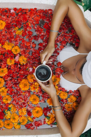 Woman relaxing in outdoor bath with flowers in Bali spa hotel.
